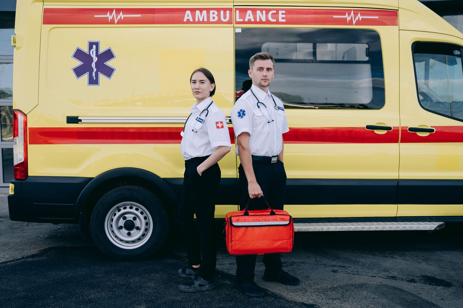 Two paramedics in uniform standing confidently beside a yellow ambulance, ready for emergency response. - Why am I being asked to enter my preferred spoken and written language?