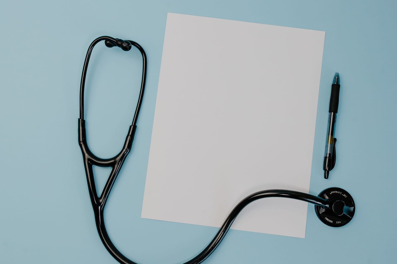 Flat lay of a stethoscope, blank paper, and pen on a blue background. - SHOP how-to guides, fact sheets, tools, and other resources for employers