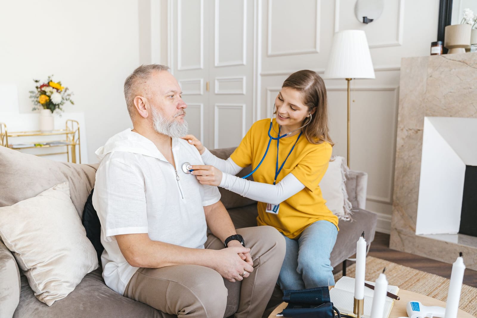 A nurse uses a stethoscope for a home check-up on a senior adult in a cozy living room. - Marketplace coverage & COVID-19