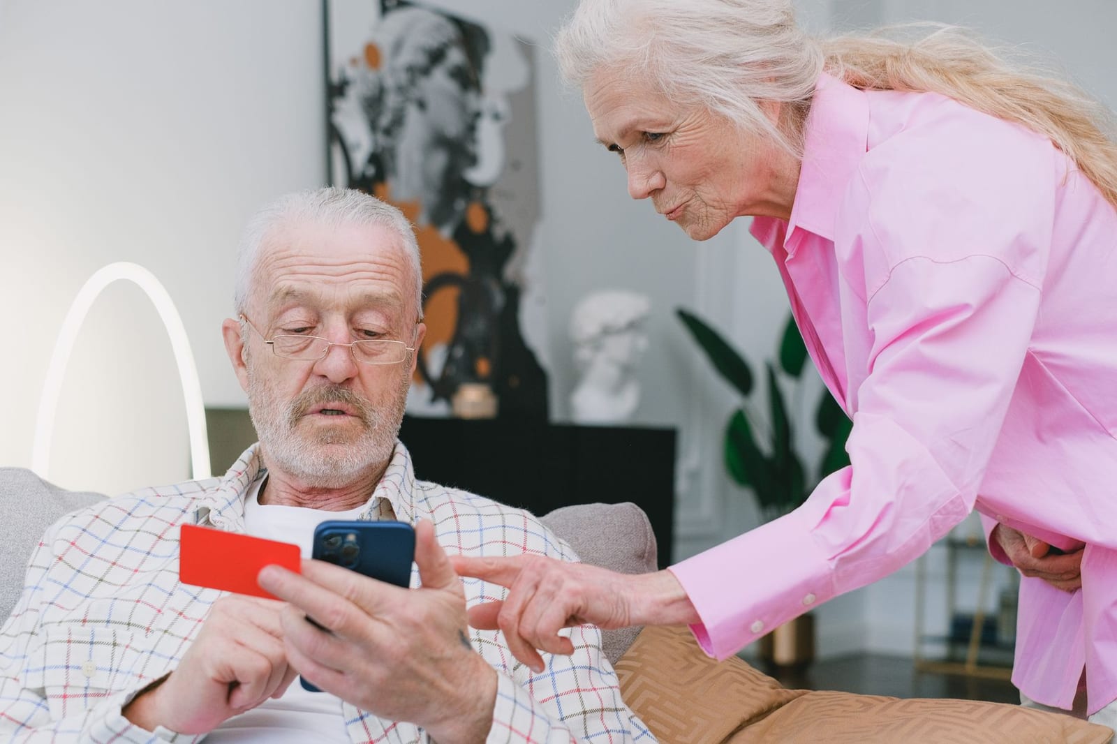 Elderly couple handling credit card transaction on smartphone indoors. - What to Do After Applying For Health Care on Paper or By Phone
