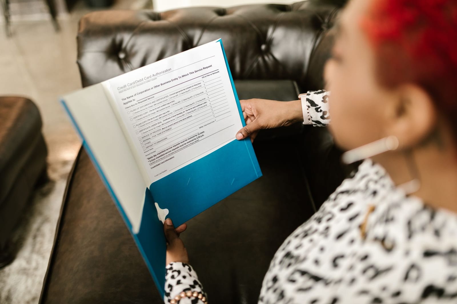 A woman sits on a couch reading a document in a blue folder. - Dental plan datasets:  Individuals & families