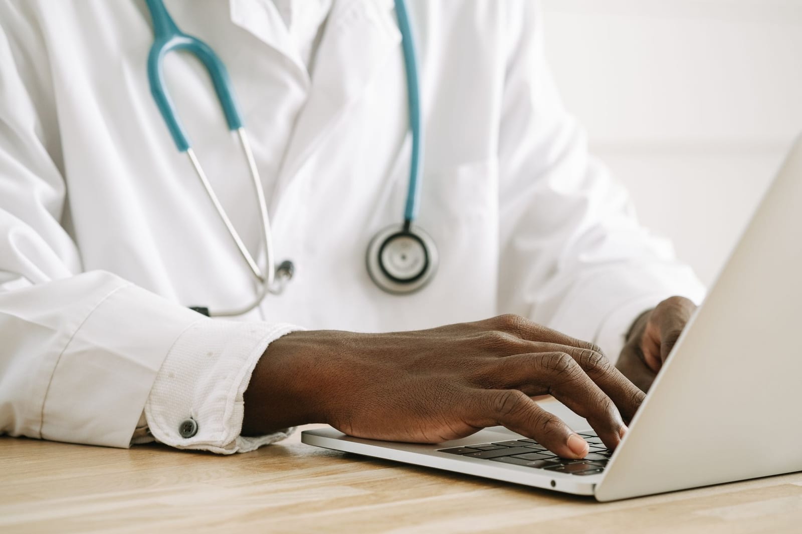Close-up of a doctor using a laptop, wearing a stethoscope and white coat. - If you had other health coverage