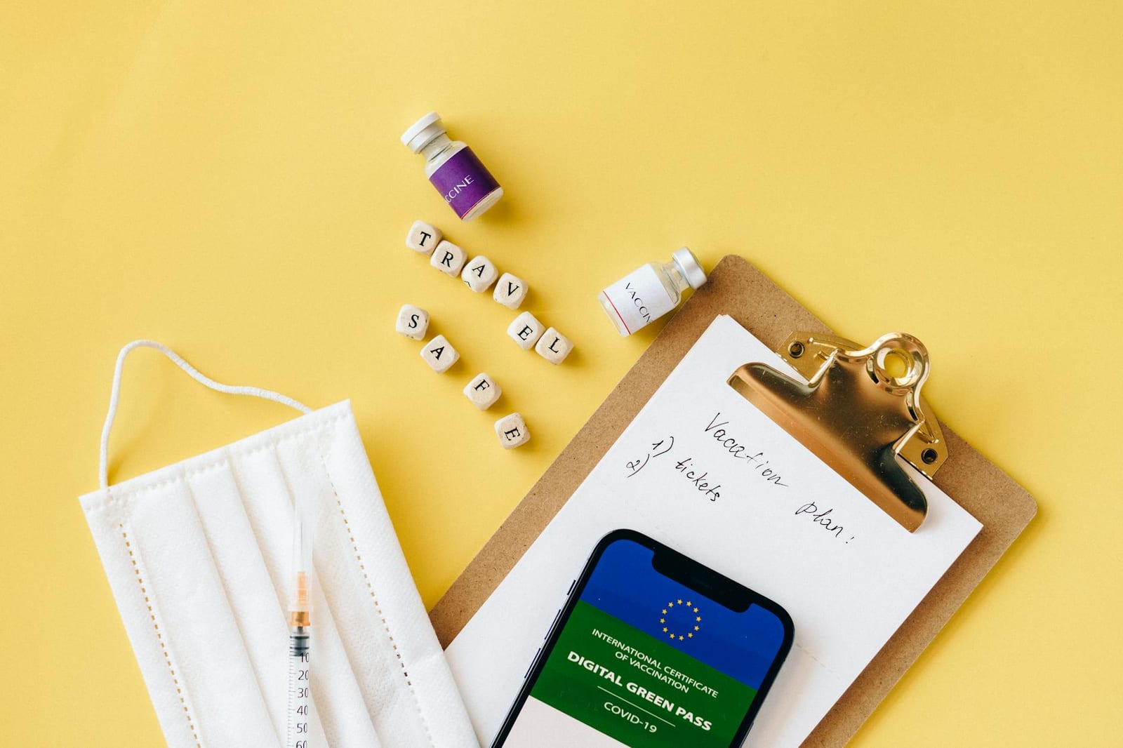 Flat lay of travel safety items: vaccine, mask, digital green pass on a vibrant yellow background. - 2019 Marketplace plan with premium tax credits