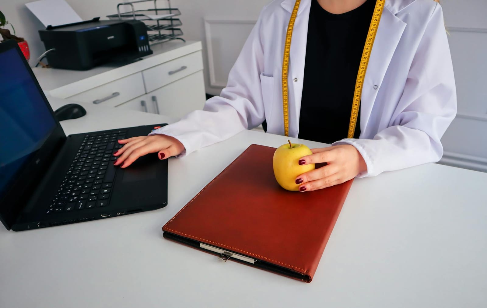A dietician sitting at a desk with a laptop and apple, symbolizing healthy working lifestyle. - Health coverage for incarcerated people