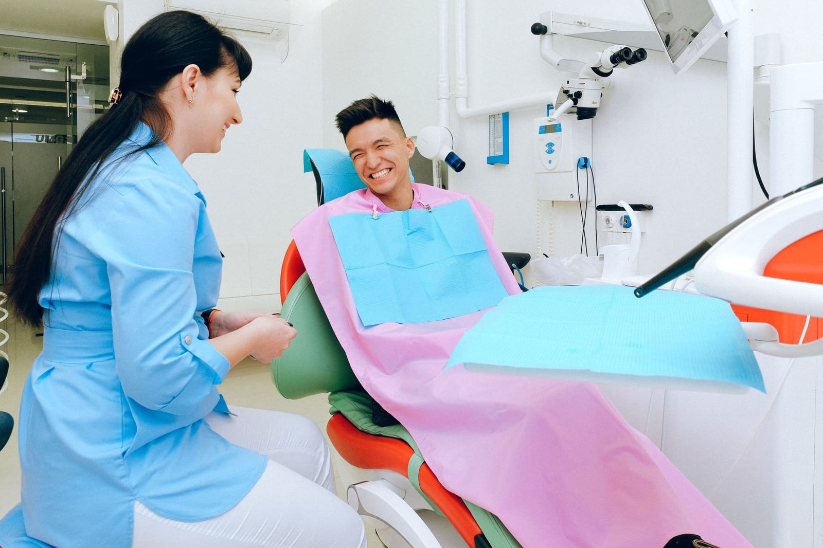 Happy ethnic guy sitting in dental chair and smiling while talking with female dentist in uniform before treatment in modern clinic - Reporting income expenses