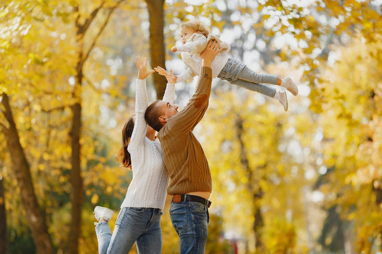 Side view of happy young parents standing close to each other while playing with cute little daughter throwing up and catching child with raised arms - 2022 SHOP dental plan information for small businesses