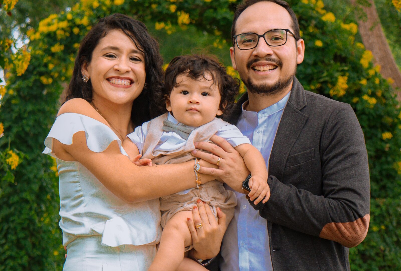 ACA / Obamacare Plans — A joyful family of three smiling outdoors in front of a green garden archway, representing ACA family health coverage.