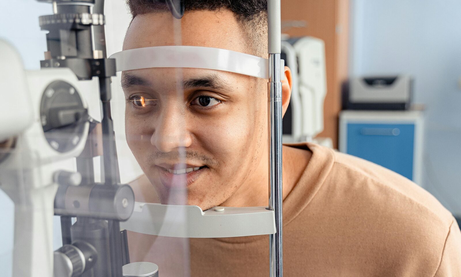 Dental & Vision — A man undergoing an eye examination at an optometrist's office with diagnostic equipment in the foreground, representing vision coverage.