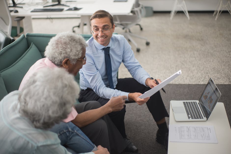 Consultant discussing financial plans with senior clients in a modern office setting, using documents and a laptop. health insurance