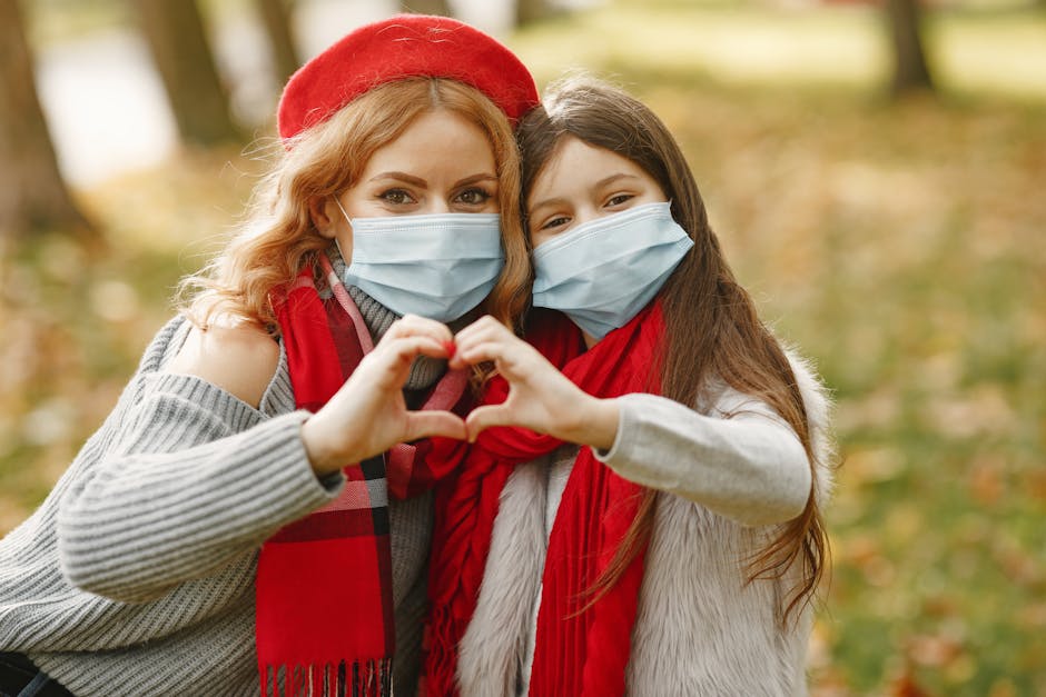 A mother and daughter wearing masks make a heart shape with their hands in a sunny park. health insurance