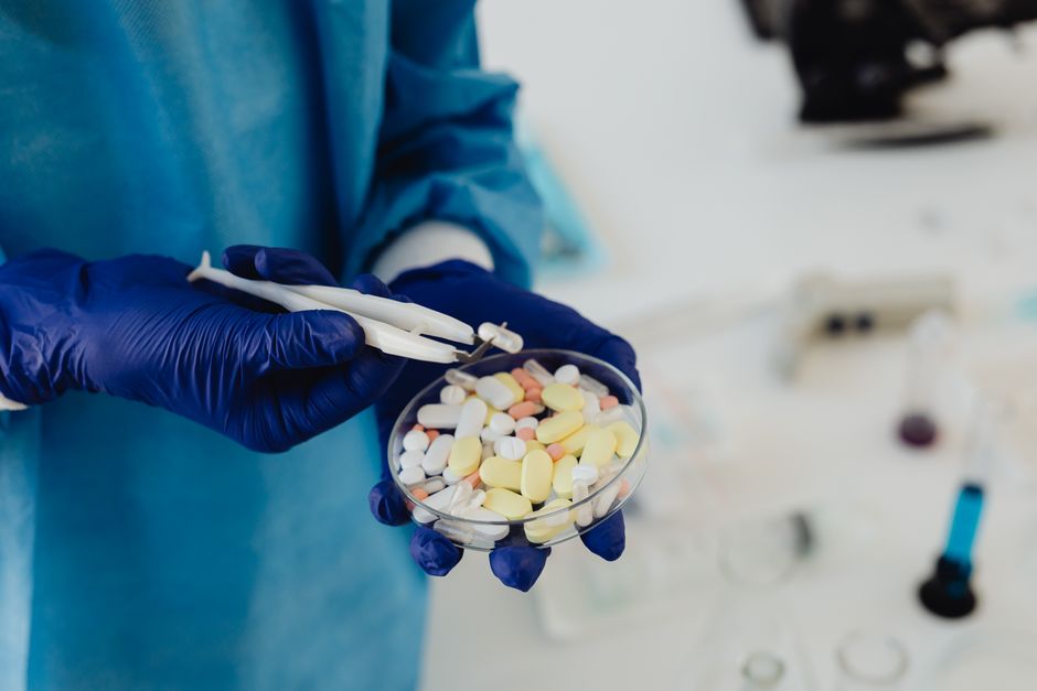 Scientist in gloves using tweezers to handle assorted pills in a petri dish. health insurance