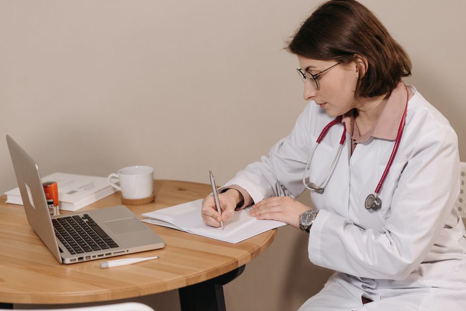 Woman doctor with stethoscope writing at desk with laptop and notes. health insurance