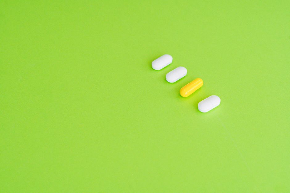 A row of white and yellow capsules on a green surface symbolizing medicine concept. health insurance