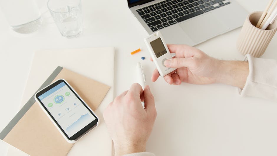 Person checking blood sugar with glucometer on a desk with smartphone and laptop nearby. health insurance