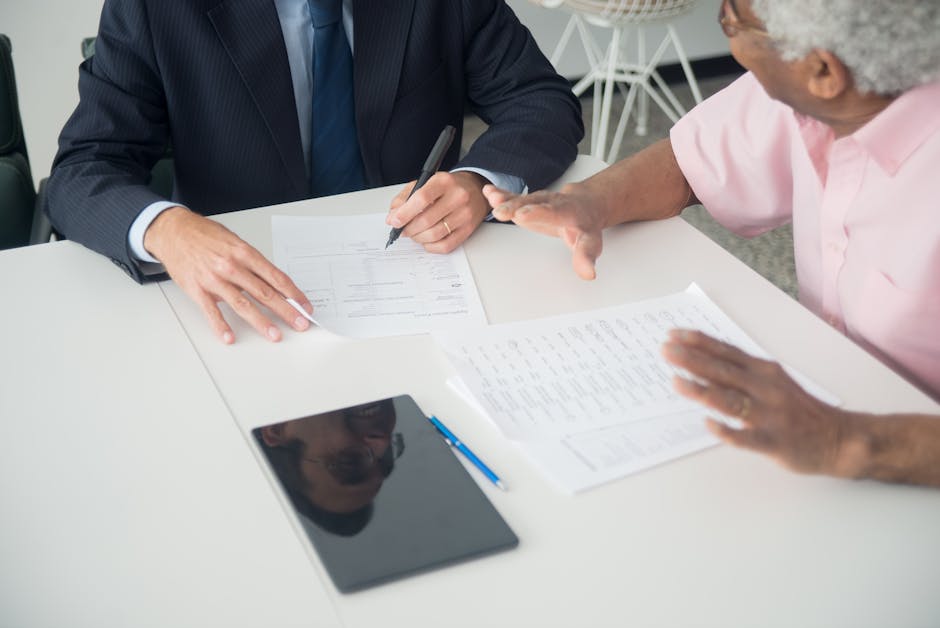 A business meeting between an elderly client and a consultant discussing documents at an office table. health insurance
