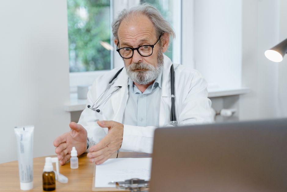An elderly doctor in a white coat conducting an online medical consultation, focusing attentively. health insurance