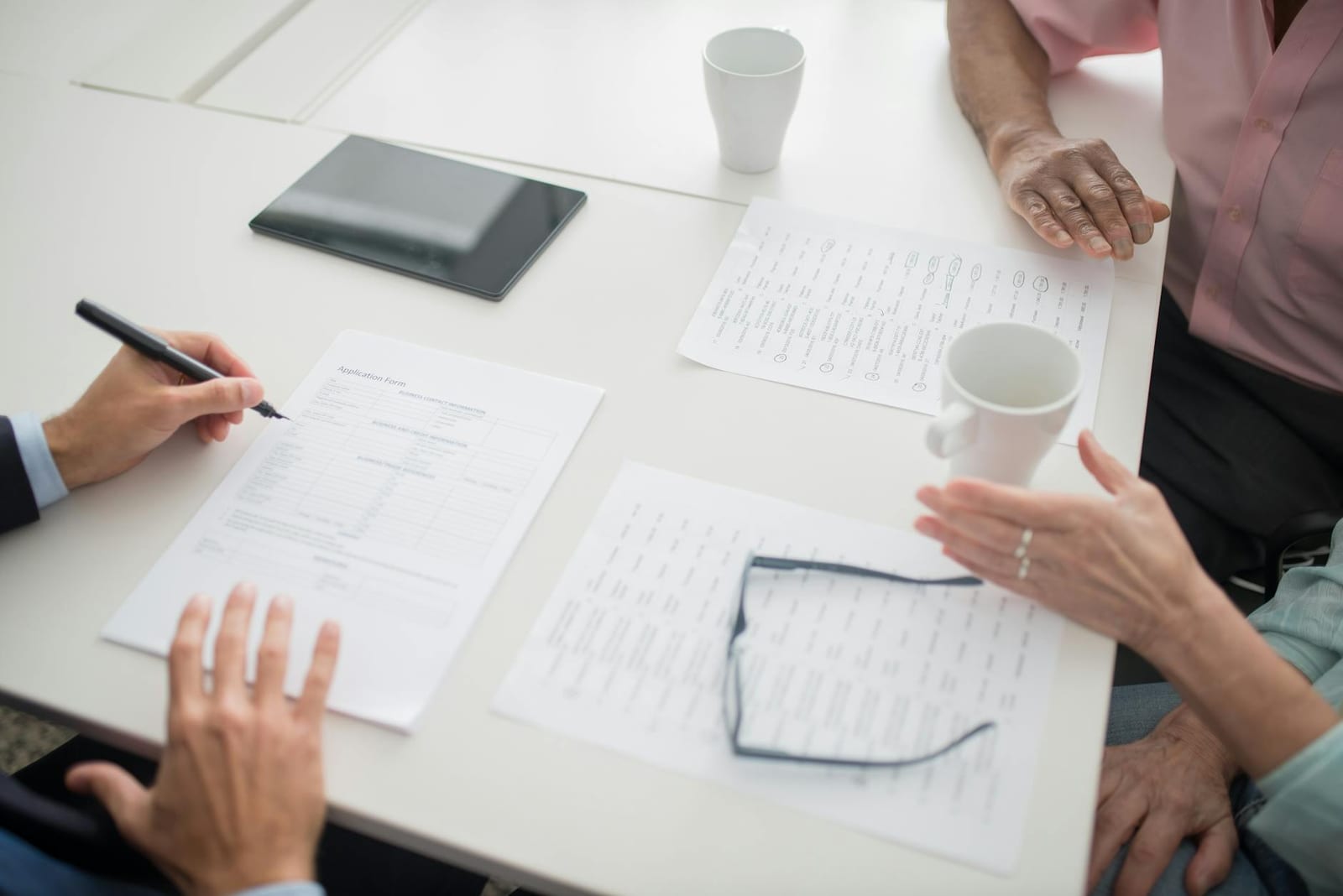 Hands writing on documents in a business meeting setup with coffee cups and tablet. health insurance
