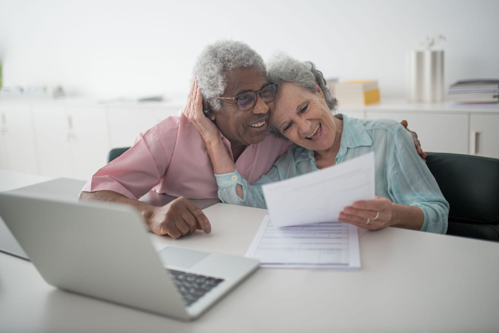 A joyful senior couple smiling while reviewing documents together at a desk with a laptop. health insurance