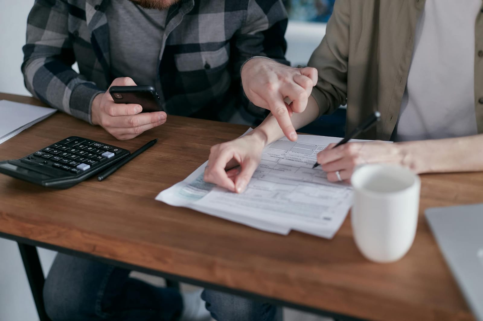 A couple analyzing financial documents and using a calculator at a home table. health insurance