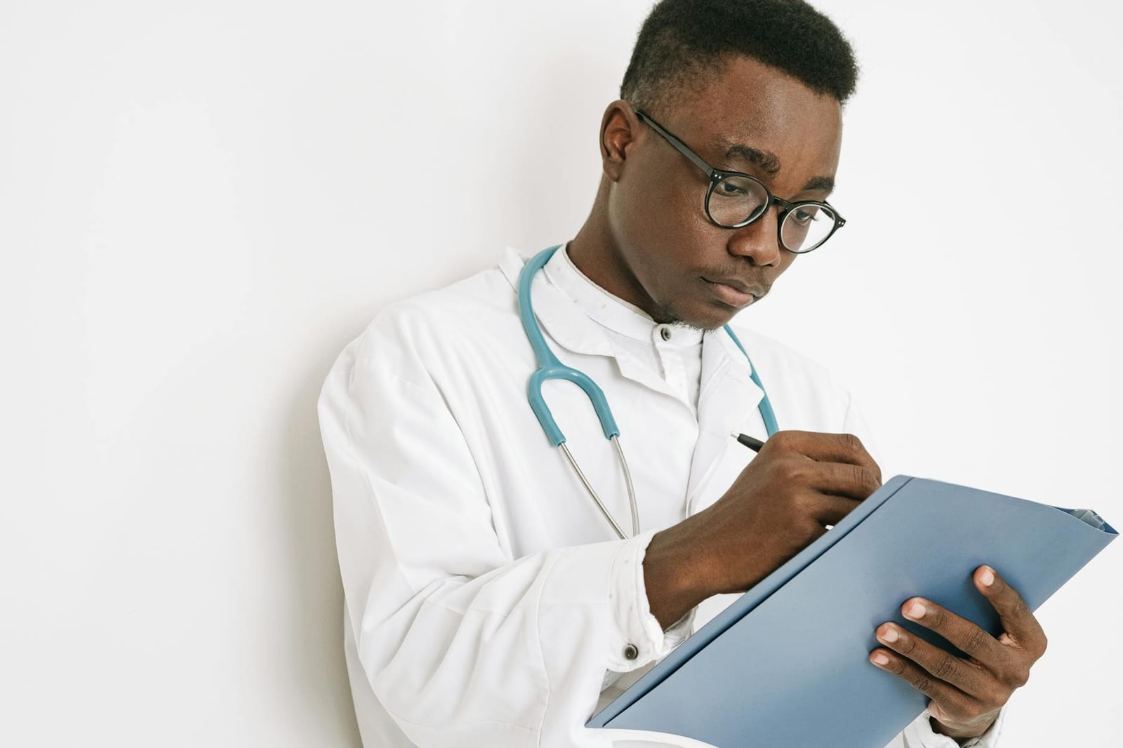 A focused doctor takes notes on a clipboard while wearing a medical gown and stethoscope. health insurance