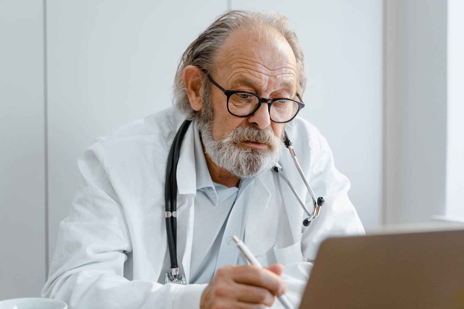 Elderly doctor with glasses and stethoscope working on a laptop in a medical office. health insurance