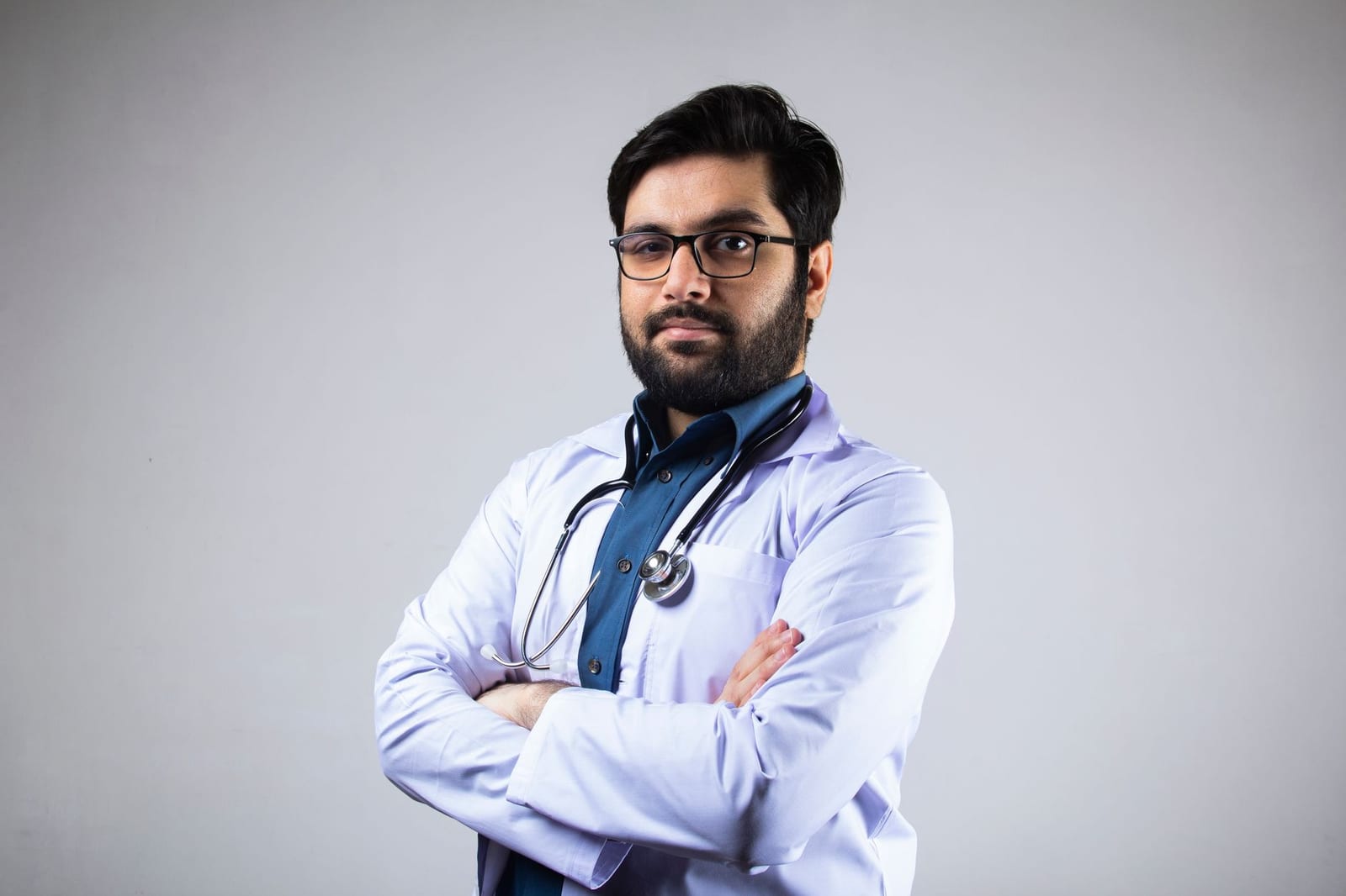 Portrait of a serious male doctor in a white coat with a stethoscope, arms crossed, studio background. health insurance