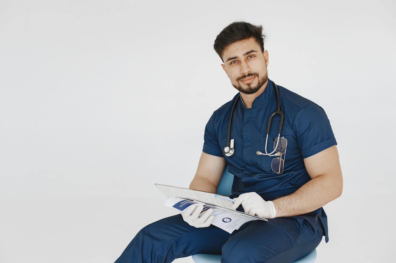 Young male doctor in blue scrubs reviewing medical records with a confident smile. health insurance