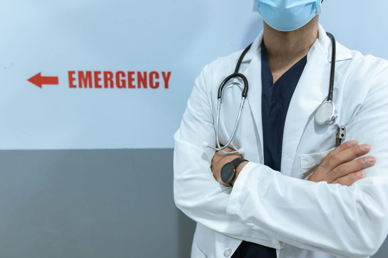Healthcare worker in emergency room with stethoscope and facemask, cross-armed posture. health insurance