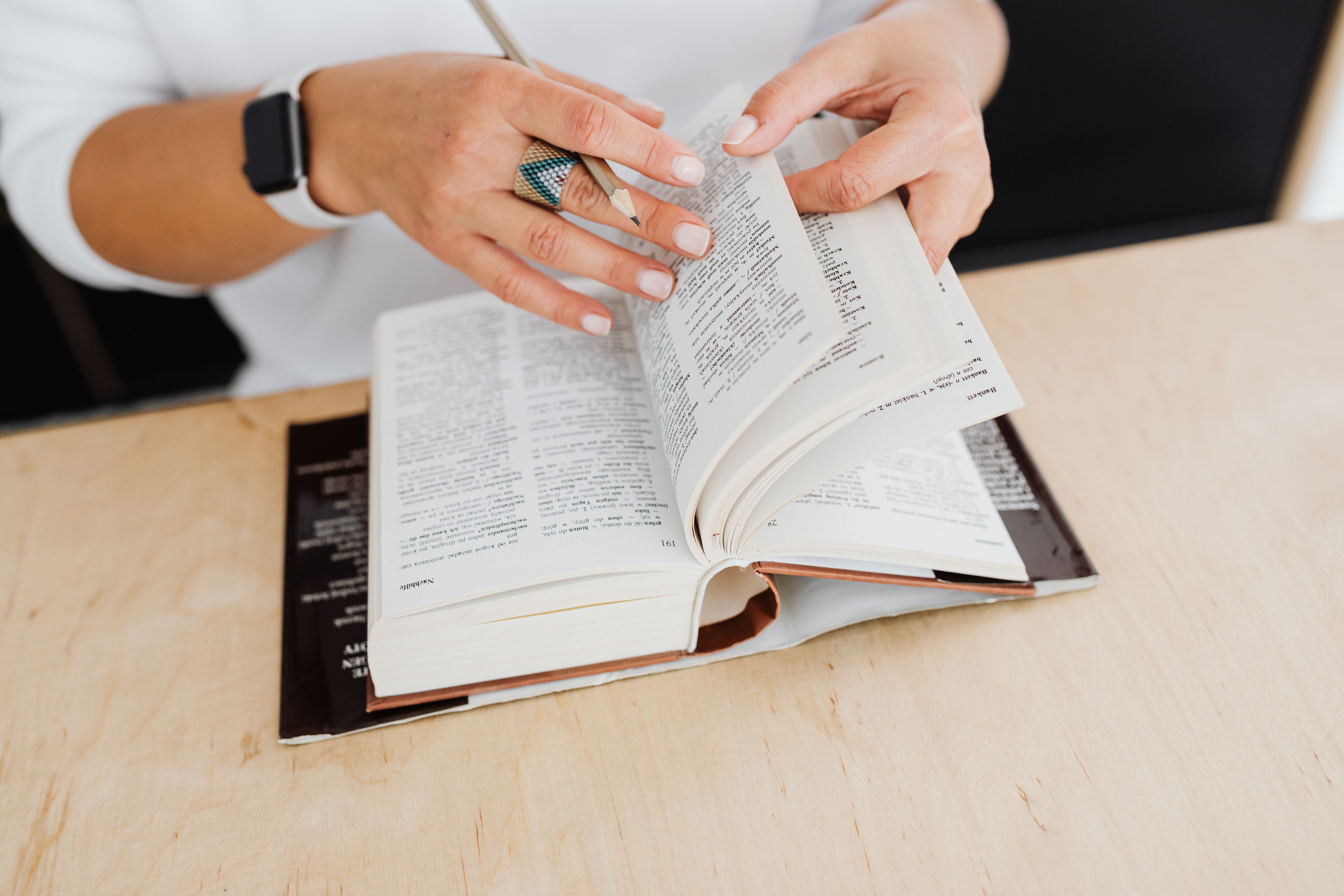 Hands flipping through a German-English dictionary with a pencil on a wooden desk, symbolizing a health insurance glossary and term lookup.